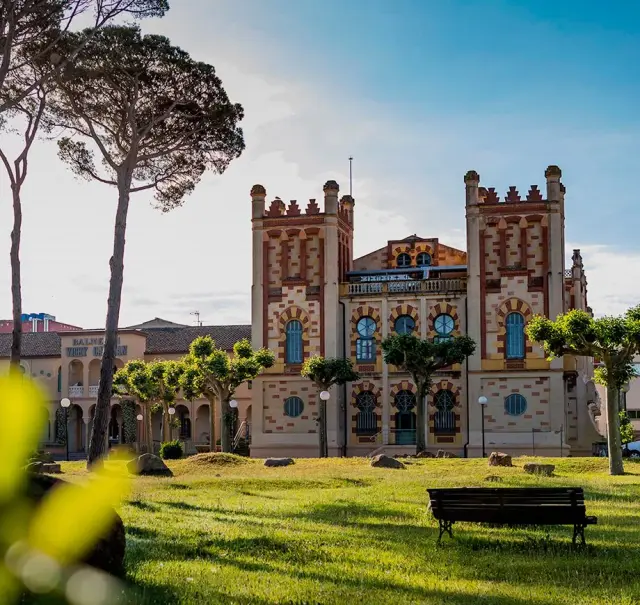Vista exterior de un edificio histórico con arquitectura modernista, rodeado de un jardín con césped, árboles