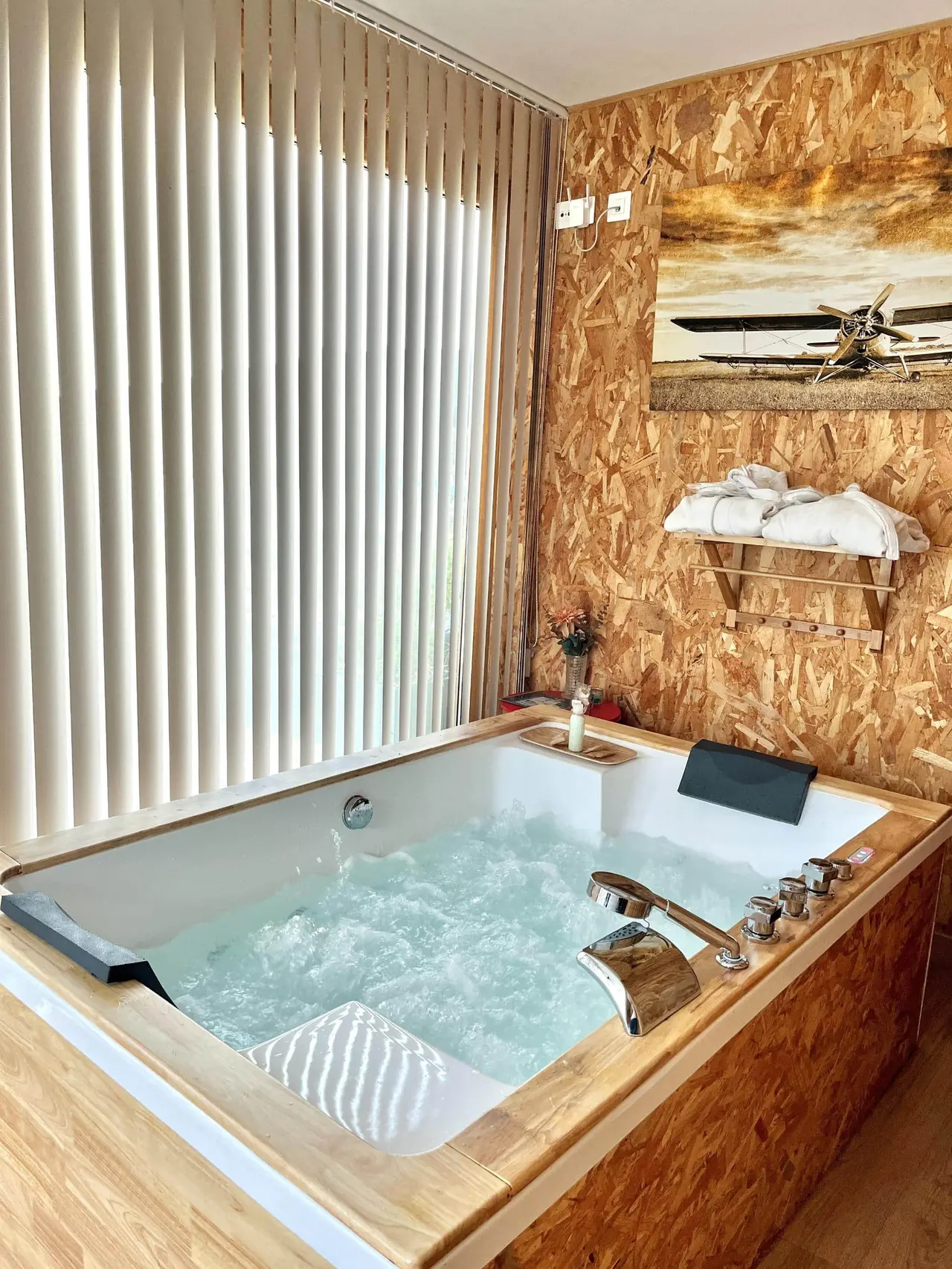 Jacuzzi rectangular empotrado en una habitación con paredes de OSB, agua burbujeante, grifo cromado y reposacabezas.