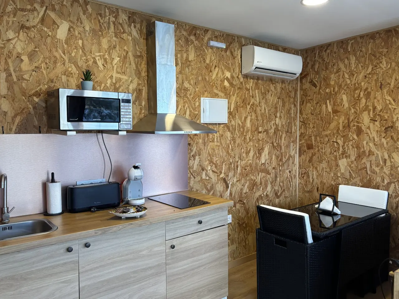 Cocina y comedor de una habitación con paredes de madera OSB, encimera de madera clara con fregadero, microondas