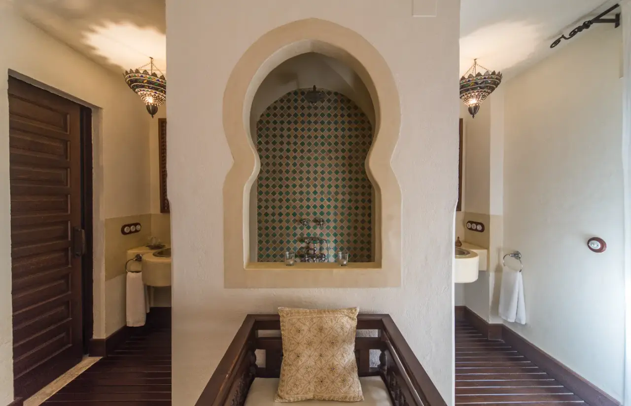 Vista de una habitación con una ducha en un nicho arqueado con azulejos de mosaico verde y negro, un banco con cojín