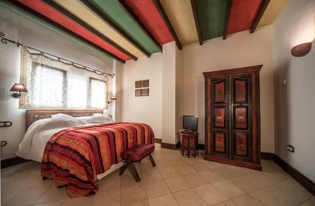 Habitación de hotel con cama grande cubierta por una colcha de rayas rojas, naranjas y blancas, cabecero de madera
