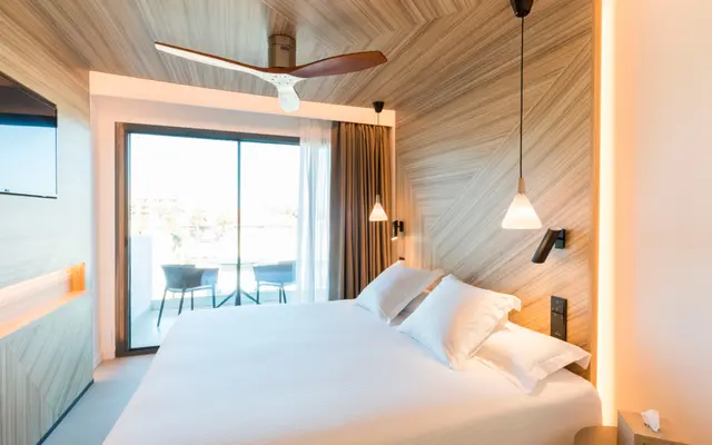 Habitación con cama grande vestida de blanco, cabecero de madera en espiga, ventilador de techo, lámparas colgantes