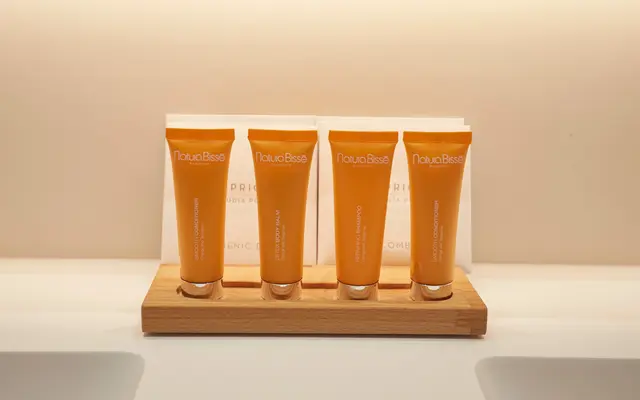 Cuatro tubos de crema corporal Natura Bissé colocados en un soporte de madera sobre un lavabo blanco.