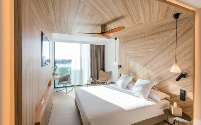 Habitación de suite con cama king size vestida de blanco, cabecero de madera en diagonal, ventilador de techo