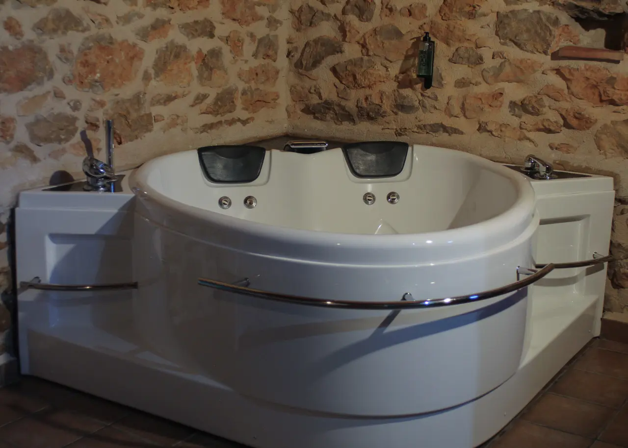 Jacuzzi blanco empotrado en una habitación con paredes de piedra rústica.