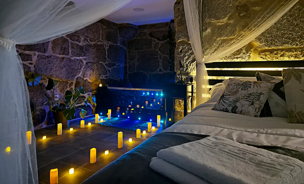 Vista de una habitación con jacuzzi privado integrado en el suelo, rodeado de velas encendidas y luces azules.
