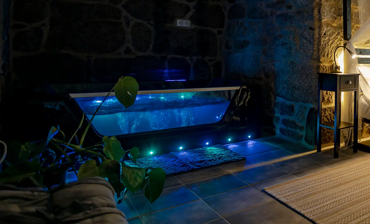 Jacuzzi rectangular empotrado en una habitación con paredes de piedra, iluminado con luces azules LED desde