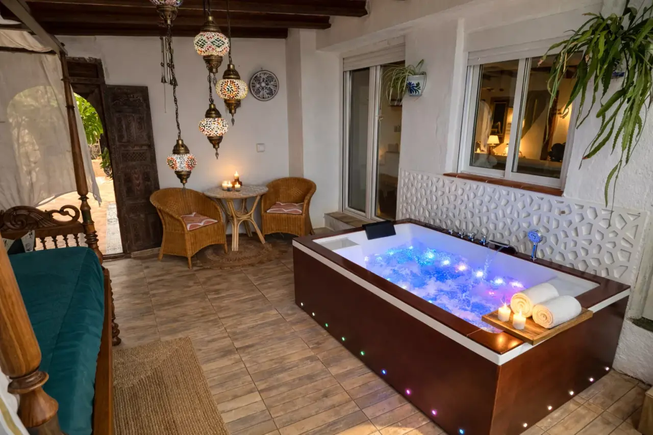 Jacuzzi iluminado en terraza privada con asientos, mesa y lámparas colgantes de estilo marroquí.