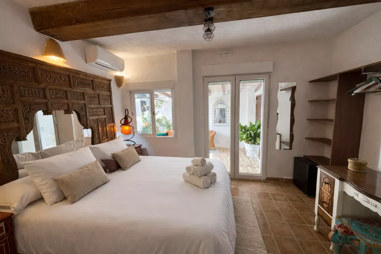 Habitación con cama grande, cabecero tallado de madera, vigas en el techo y puertas de cristal que dan