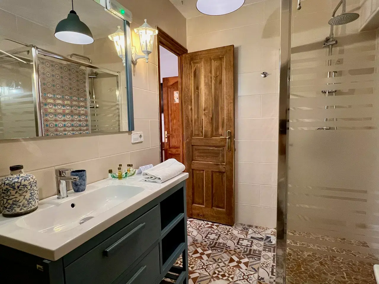 Baño con lavabo, espejo grande, ducha y puerta de madera que da al exterior.
