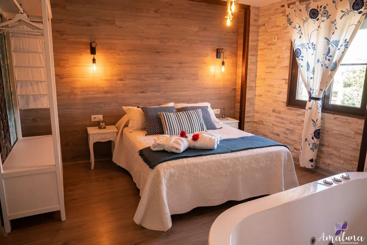 Habitación con cama doble, bañera de hidromasaje en primer plano y paredes de madera y piedra.