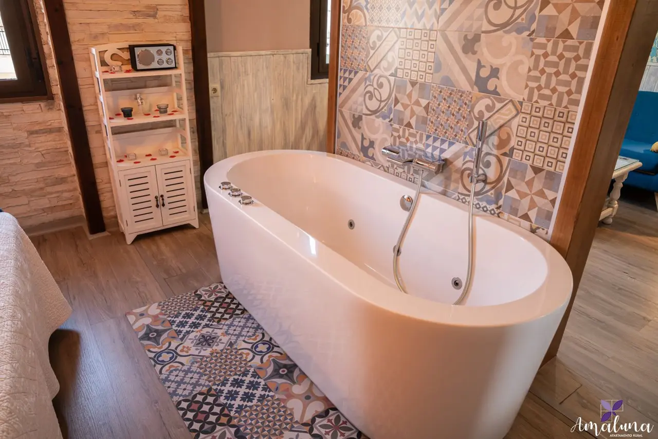 Bañera de hidromasaje blanca ovalada en habitación con suelo de madera y pared decorada con azulejos de patrones