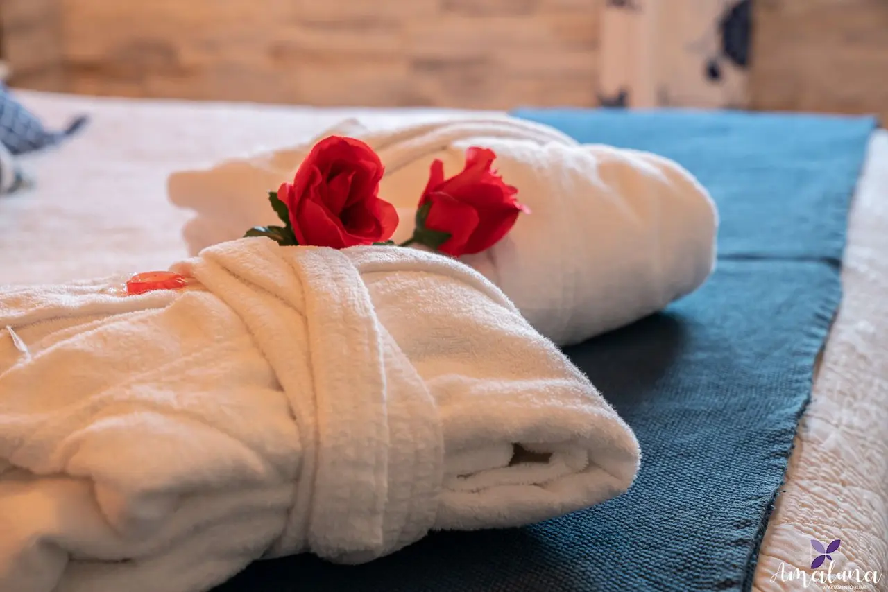 Toallas blancas enrolladas con rosas rojas sobre una superficie azul en una habitación.