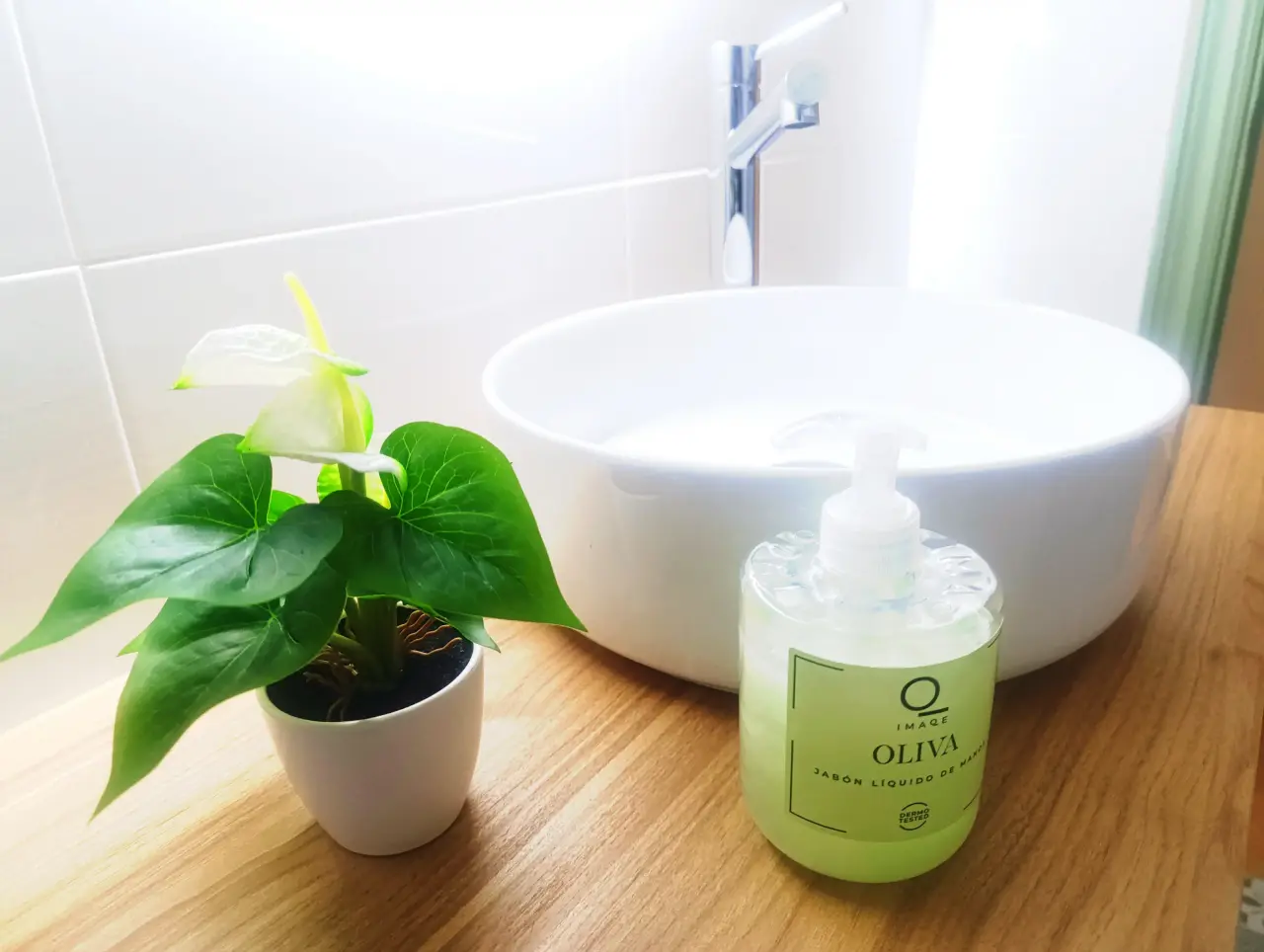 Detalle de un lavabo redondo blanco sobre encimera de madera, con un grifo cromado, una planta de anturio en maceta