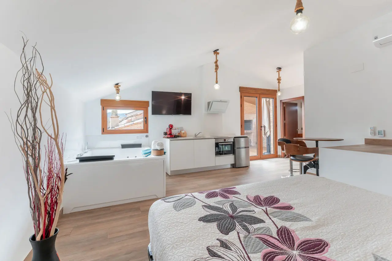 Interior de un apartamento con una bañera de hidromasaje blanca rectangular visible en la zona de estar, cama