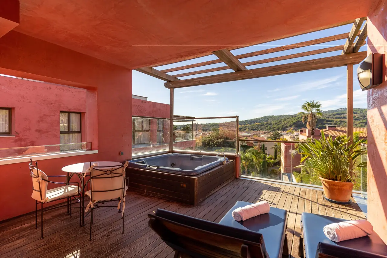 Jacuzzi rectangular empotrado en una terraza privada de madera con pérgola, rodeado de paredes de color terracota