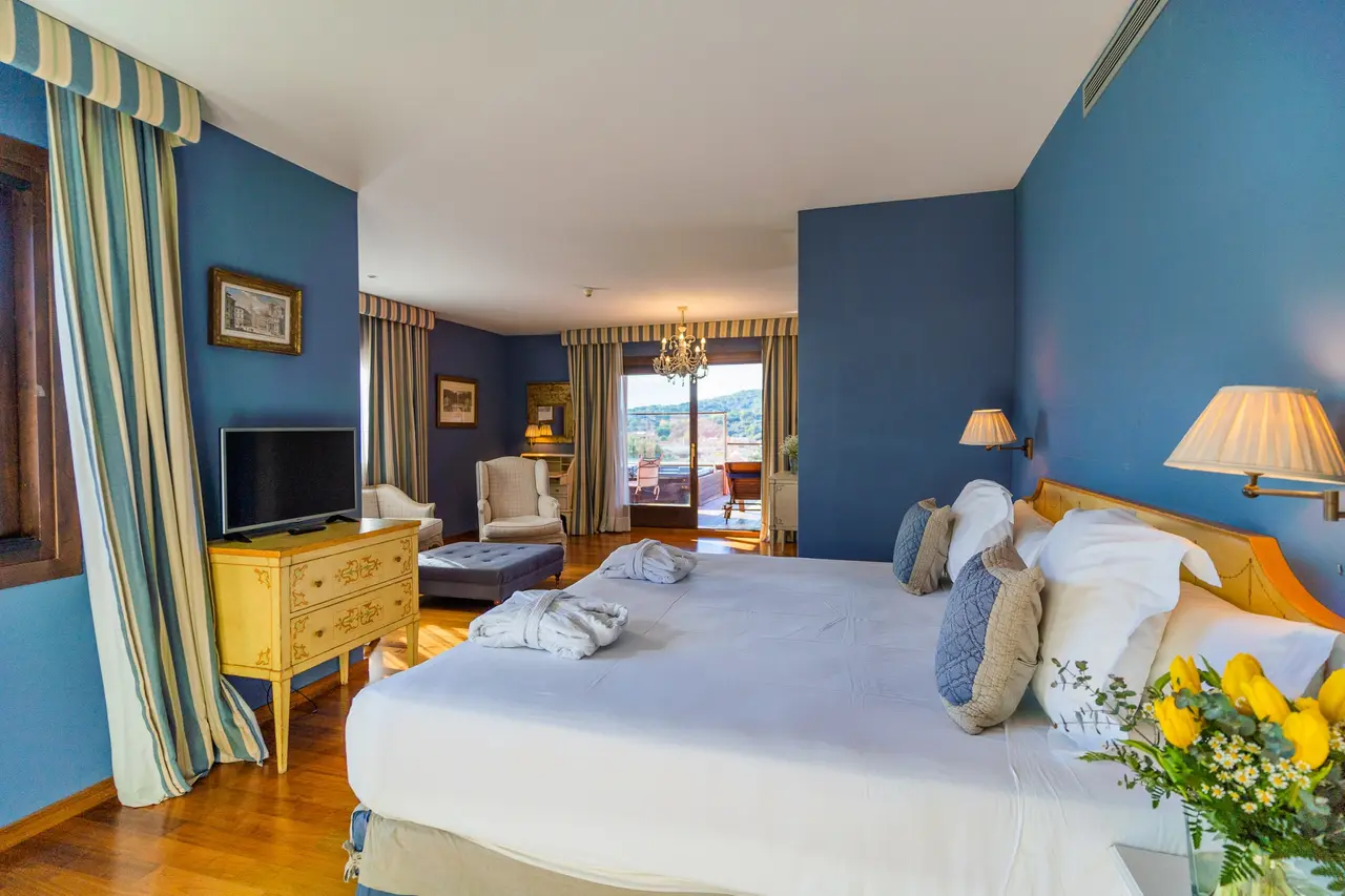 Vista de una suite de hotel con paredes azules, una gran cama con almohadas y ropa de cama blanca, un televisor