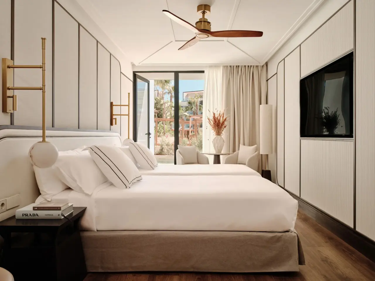 Habitación junior suite con cama king size vestida de blanco, mesita de noche con libro, lámparas de pared, techo