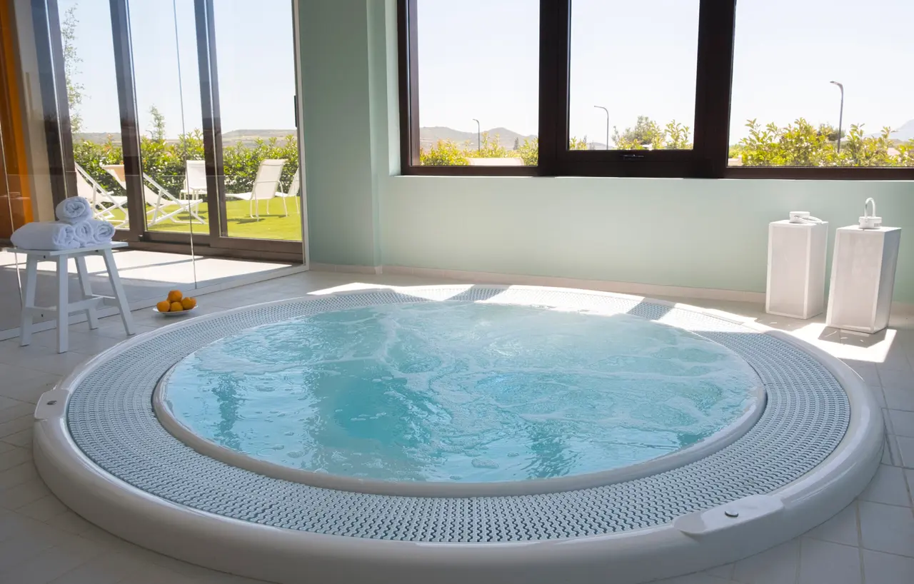 Jacuzzi circular empotrado en el suelo con agua azul clara en movimiento, rodeado de un borde de rejilla blanca.