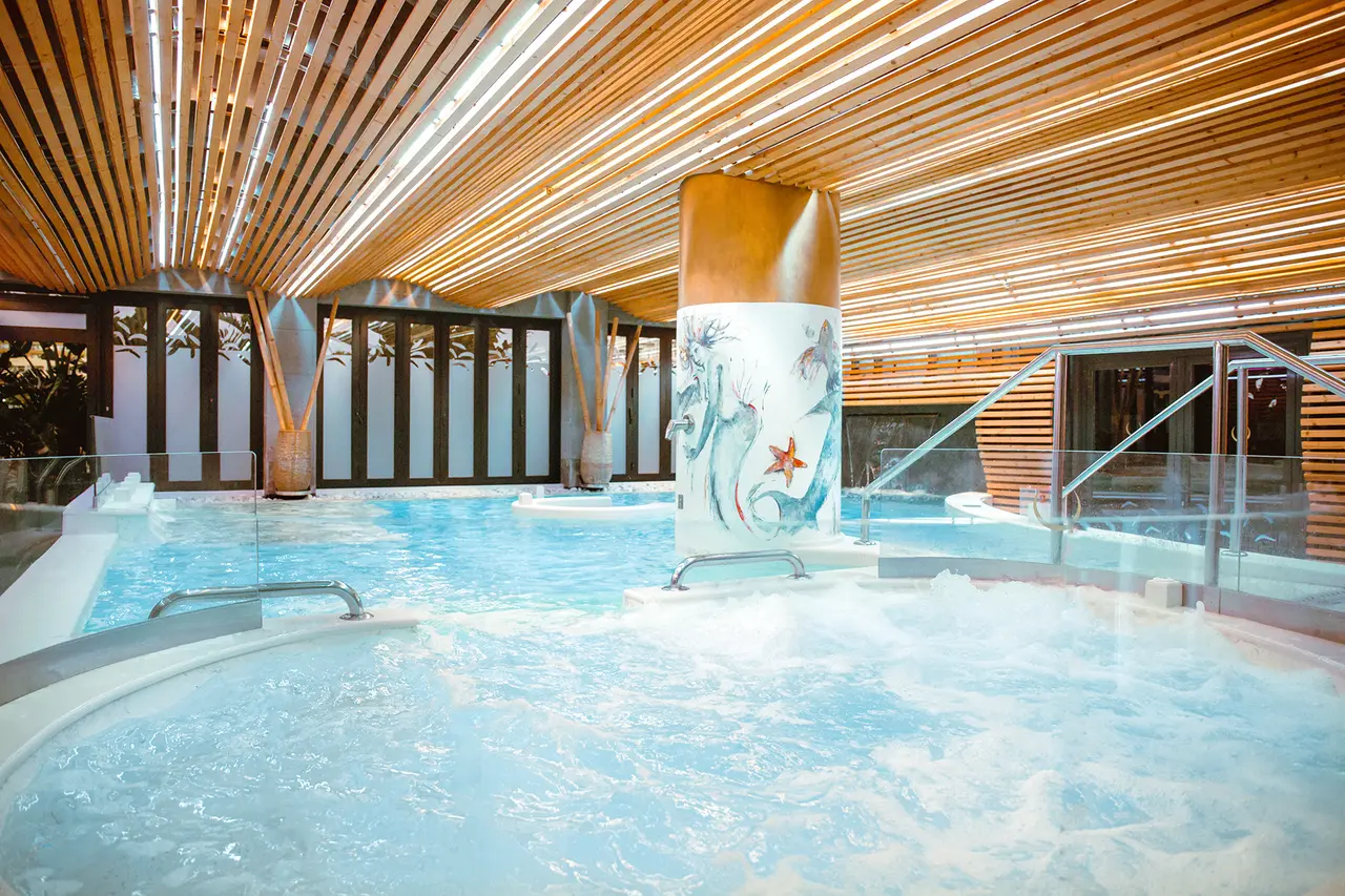 Jacuzzi circular con agua burbujeante en un spa interior con techo de listones de madera y columna decorada