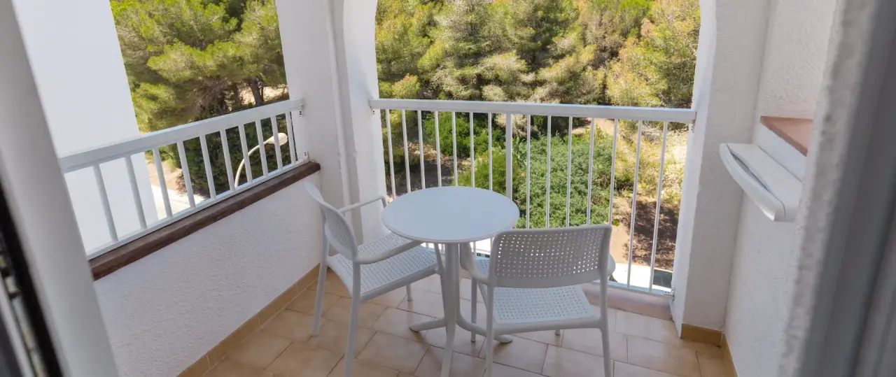 Balcón de suite con suelo de terrazo, mesa redonda blanca y dos sillas de plástico blanco, barandilla blanca y vistas