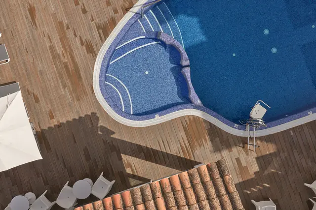 Vista aérea de una piscina exterior con forma irregular y zona de jacuzzi integrada, rodeada de tarima de madera