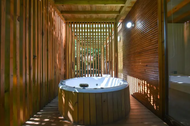 Cabanas de Apriscos — Cabañitas del Bosque: Jacuzzi circular de madera en un pasillo techado con paredes de listones de madera, piso de madera y luz natural filtrad
