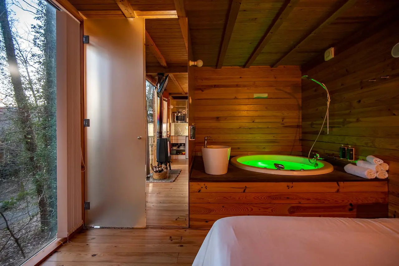 Interior de una cabaña de madera con un jacuzzi redondo iluminado en verde, situado sobre una plataforma de madera