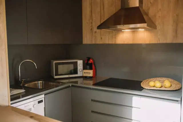 Cocina compacta con encimera en L de color gris, fregadero de acero inoxidable con grifo curvo, microondas blanco