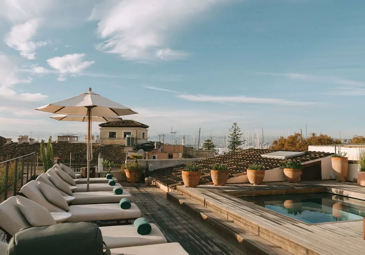 Terraza en la azotea con piscina rectangular, tumbonas acolchadas alineadas bajo una sombrilla grande, macetas