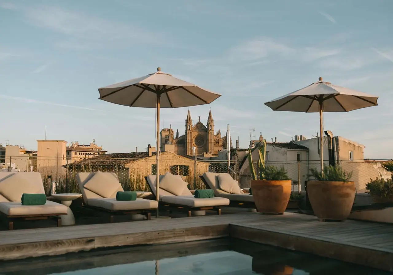 Terraza con piscina en la azotea, tumbonas con cojines, sombrillas y macetas con plantas, con vistas a la catedral