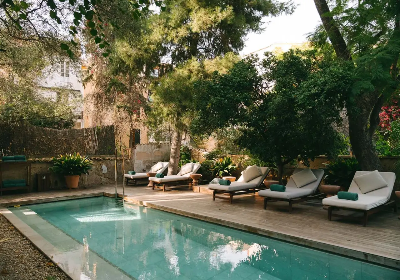Piscina rectangular al aire libre con agua turquesa, rodeada de una terraza de madera con varias tumbonas acolchadas