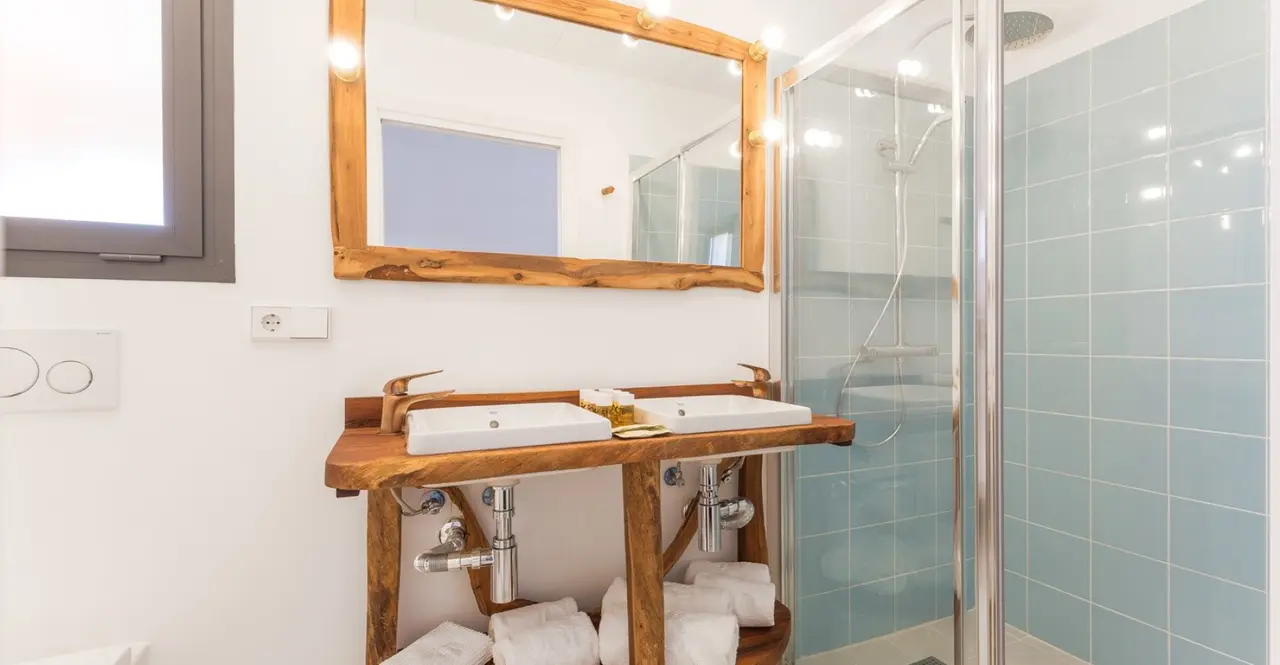 Baño con doble lavabo sobre encimera de madera rústica, espejo grande con marco de madera, ducha con mampara