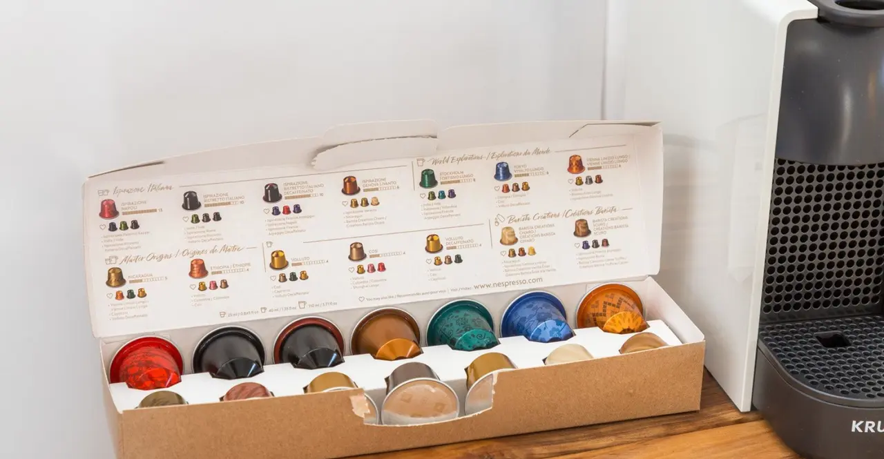 Caja abierta de cápsulas de café de diferentes sabores y colores colocada sobre una encimera de madera