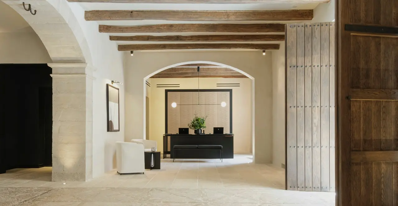 Vestíbulo de entrada con arcos de piedra, vigas de madera y recepción al fondo en un hotel rústico.