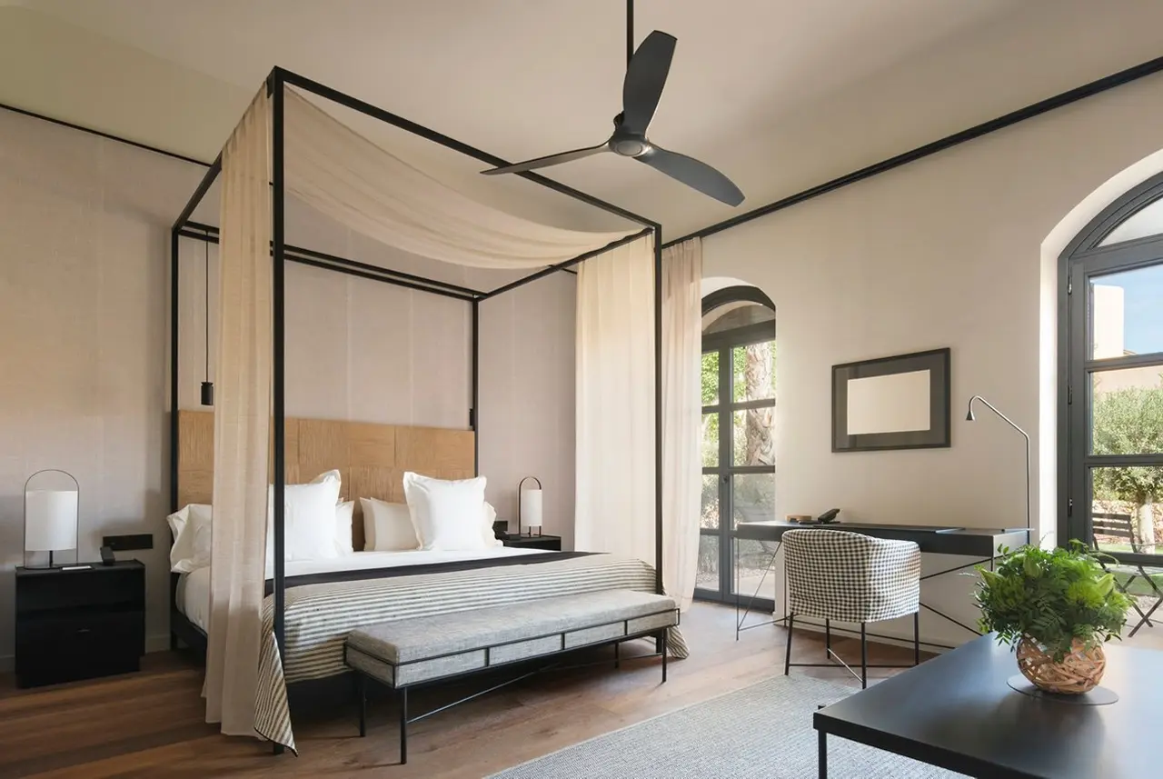 Habitación con cama de dosel, escritorio, sillas y gran ventanal con vistas al exterior.