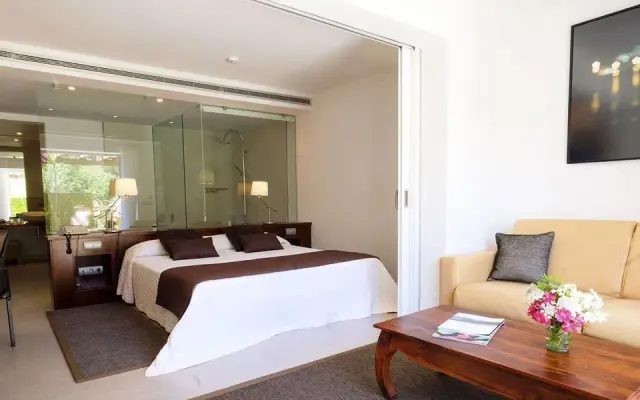 Vista de una habitación rural con cama doble, sofá beige, mesa de centro de madera y puerta corredera que da al baño