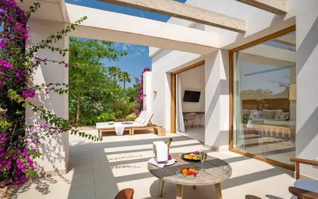 Terraza exterior de una habitación rural con suelo de baldosas claras, mesa redonda de madera con frutas, bebida