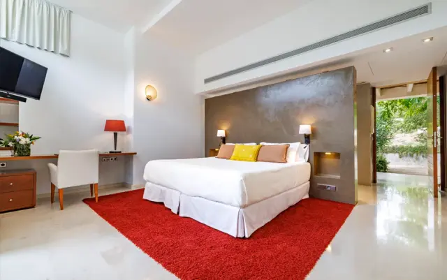 Habitación rural con cama king size vestida de blanco, alfombra roja, escritorio con silla, televisor en la pared