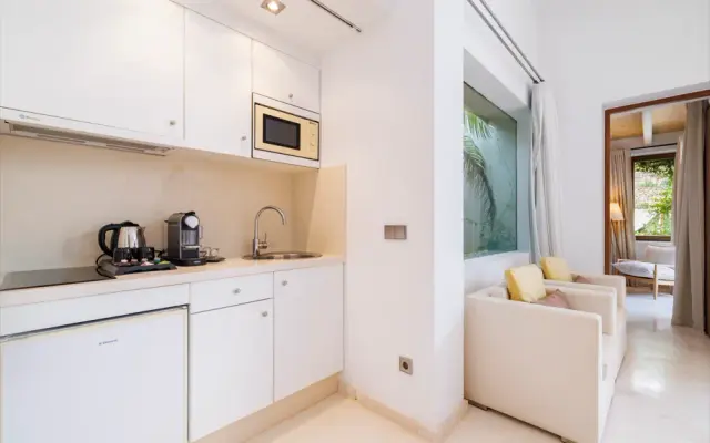 Interior de una habitación rural con zona de cocina equipada con armarios blancos, microondas, fregadero, cafetera