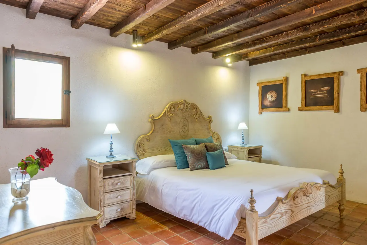 Habitación con cama de madera tallada, cabecero dorado, mesitas de noche, vigas de madera en el techo y suelo