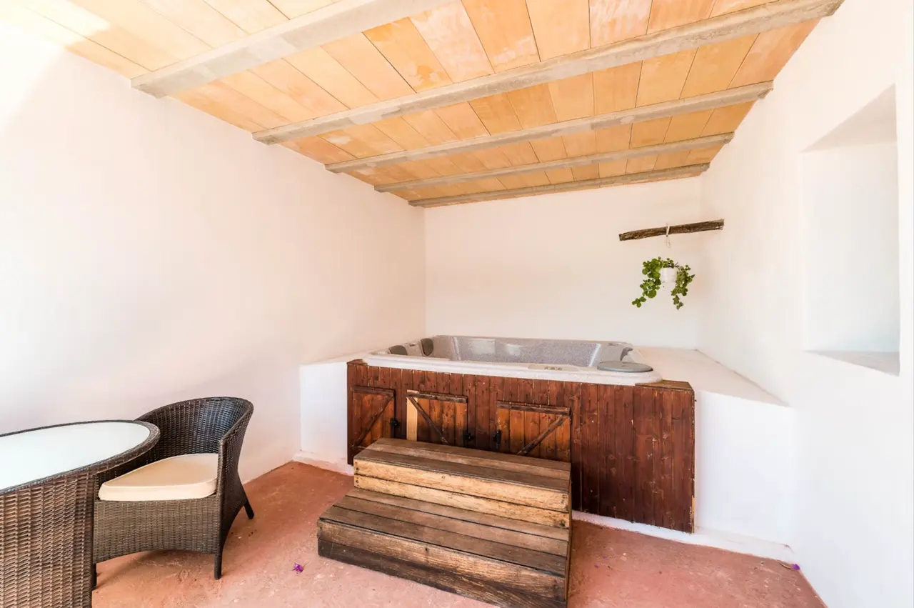 Habitación con jacuzzi empotrado en estructura de madera, dos escalones de acceso, silla de mimbre y techo