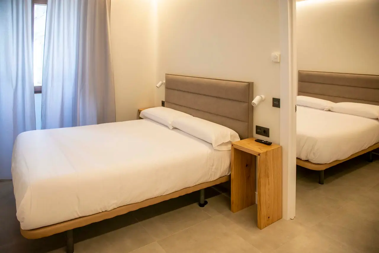 Habitación con dos camas individuales, cabeceros tapizados en beige, mesita de noche de madera y cortinas claras