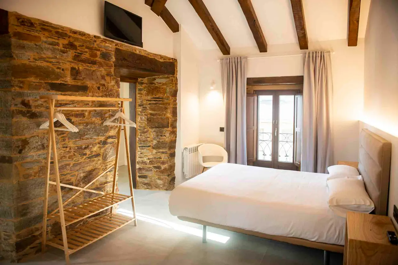 Habitación de suite con cama doble, cabecero de madera, pared de piedra rústica, perchero de madera, televisor montado