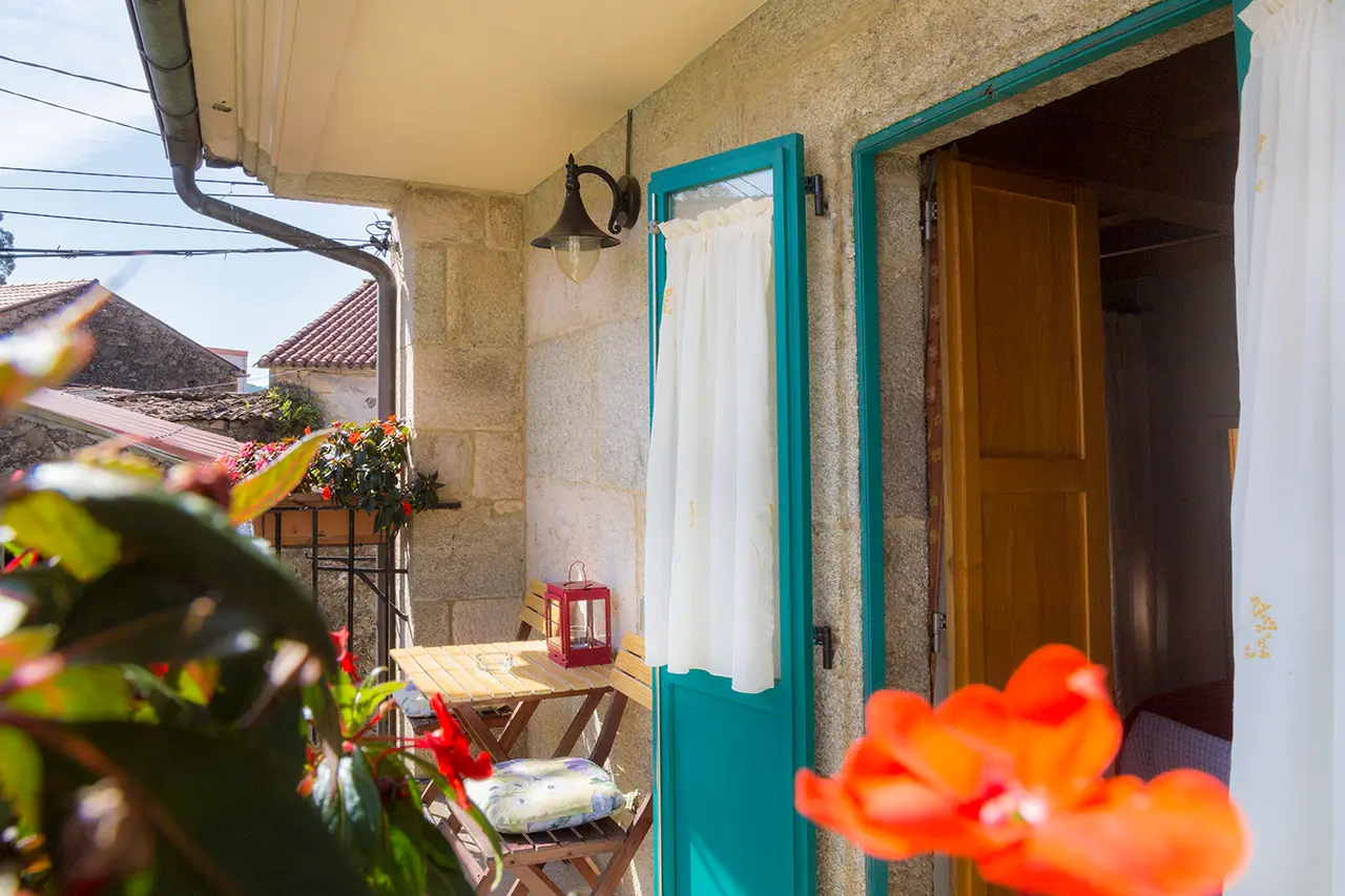 Vista exterior de una entrada a una habitación con puerta de madera y marco turquesa, cortina blanca, pequeño patio