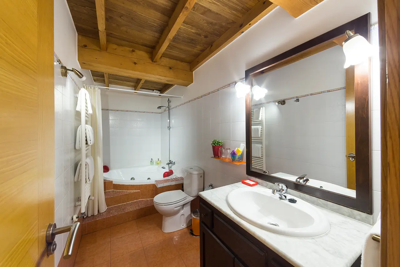 Baño de la habitación con bañera de hidromasaje en el fondo, inodoro, lavabo con encimera de mármol y espejo grande