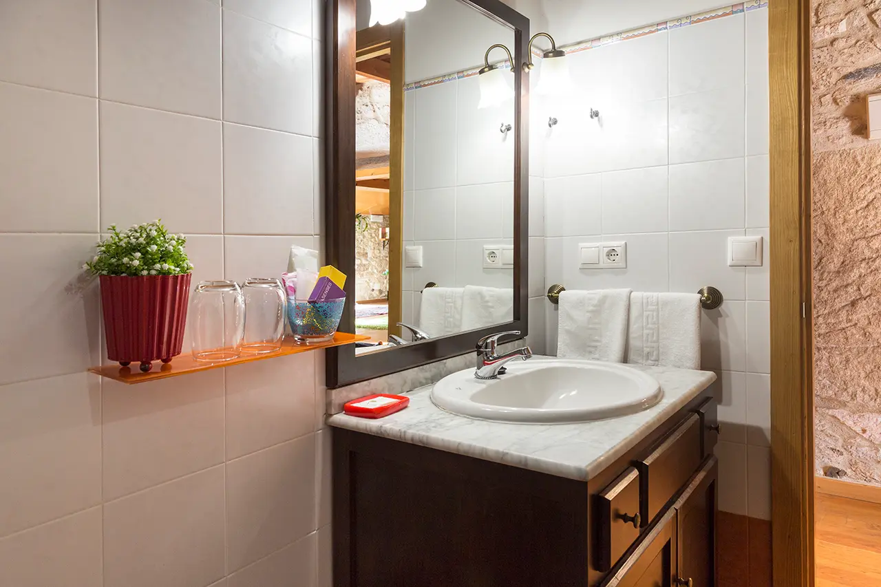 Baño con lavabo de cerámica blanca sobre encimera de mármol, grifo cromado, espejo rectangular grande con iluminación