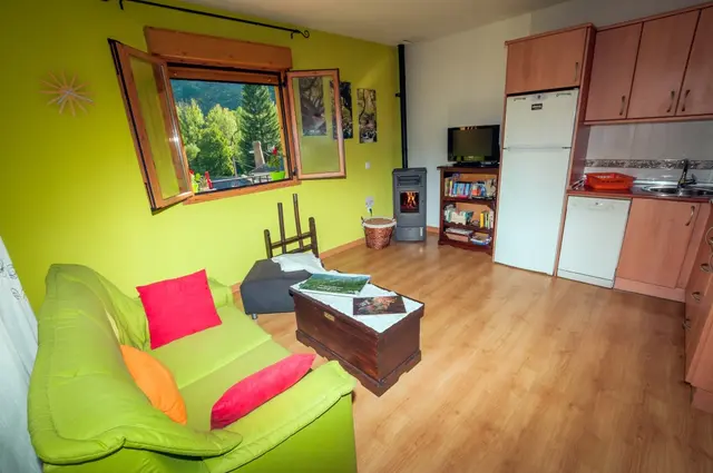 Interior de una habitación con paredes verdes y blancas, sofá verde con cojines rojos y naranjas, mesa de centro