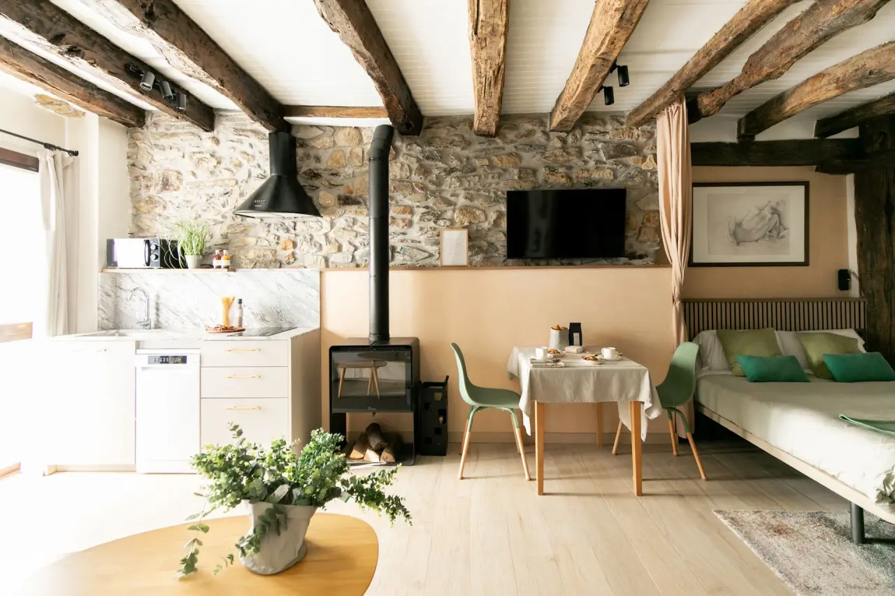 Interior de un loft con paredes de piedra, vigas de madera en el techo, cocina equipada a la izquierda, estufa