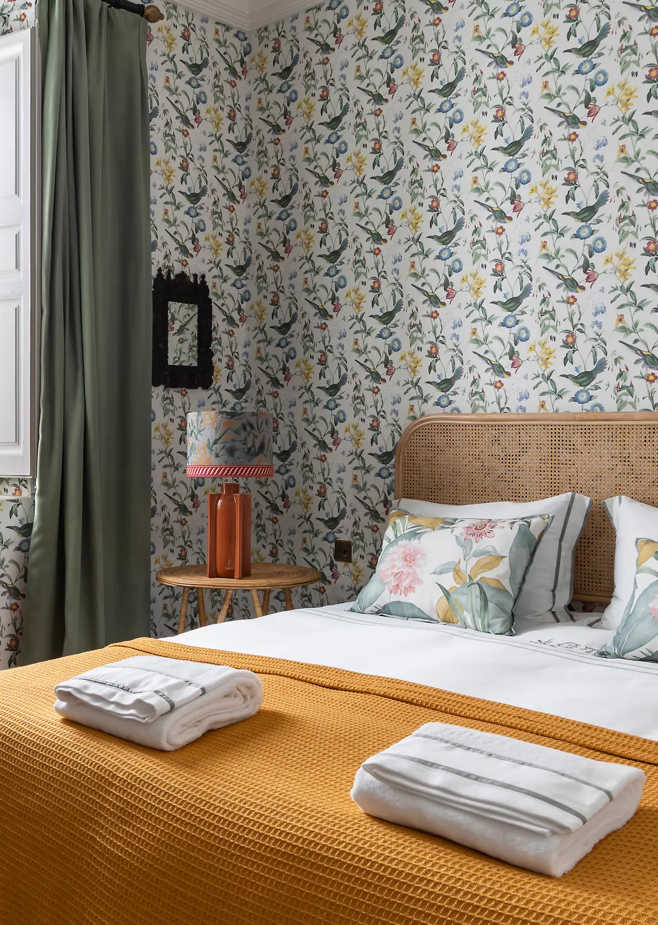 Habitación con cama grande, cabecero de mimbre, colcha amarilla y toallas blancas dobladas.